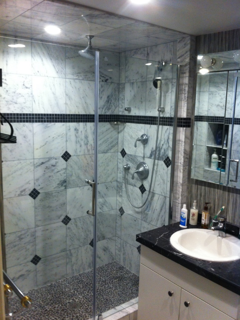 New shower with marble tiles and clear glass door.